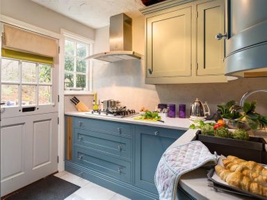 A kitchen with blue and beige cabinets a door with window panes and croissants on the counter at Acorn Cottage in Grasmere