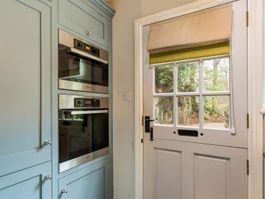 A kitchen corner with built-in double ovens next to a door with glass window panes at Acorn Cottage in Grasmere