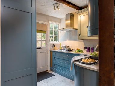 A kitchen with blue cabinets a gas stove a tray of croissants a window and a door at Acorn Cottage in Grasmere
