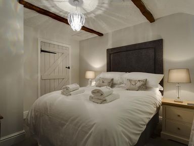 A bedroom with a bed with folded towels on it bedside tables with lamps and a wooden door at Acorn Cottage in Grasmere