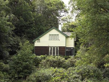 A house with white and dark wood siding surrounded by dense green trees and shrubs at Acorn Cottage in Grasmere