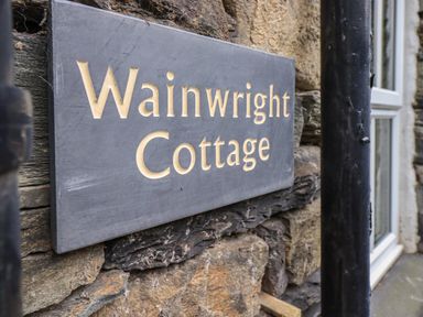 A close up of a stone wall with a sign reading Wainwright Cottage in Ambleside
