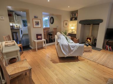 A living room with a sofa facing a wood burning stove a small table chairs and a dining area in the background at Wainwright Cottage in Ambleside