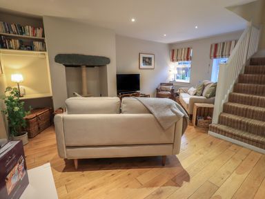 A living room with two sofas a television a bookcase and stairs at Wainwright Cottage Ambleside