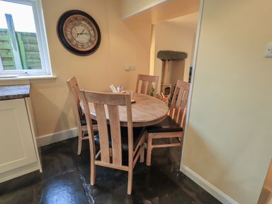 A dining area with a round wooden table and four chairs next to a window and a wall clock at Wainwright Cottage in Ambleside