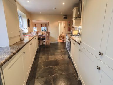 A kitchen with cabinets on both sides a stove and oven on the right and a dining table with chairs in the background at Wainwright Cottage in Ambleside