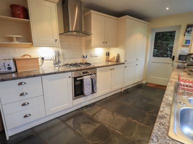 A kitchen with white cabinets stone floor and a door at Wainwright Cottage in Ambleside