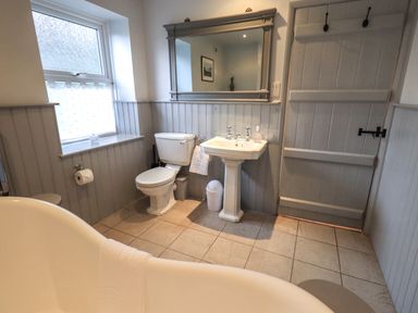 A bathroom with a toilet sink bathtub large mirror window and a wooden door at Wainwright Cottage in Ambleside