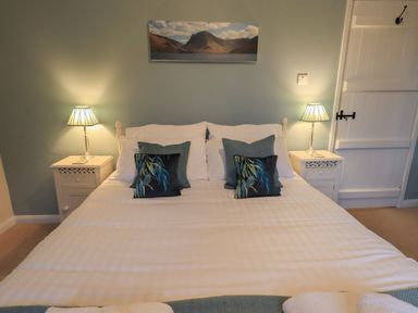 A bedroom with a double bed two bedside tables lamps and a landscape picture on the wall at Wainwright Cottage in Ambleside