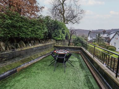An outdoor patio with artificial grass and metal chairs around a round mosaic table at Wainwright Cottage in Ambleside