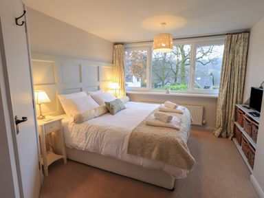 A bedroom with a bed a bedside table lamps and a window with curtains at Wainwright Cottage in Ambleside