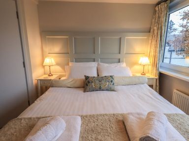 A bedroom with a large bed two bedside tables with lamps and rolled towels on the bed at Wainwright Cottage in Ambleside