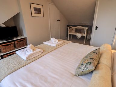 A bedroom with a bed with folded towels a television on a shelf with wicker baskets and a bench with cushions at Wainwright Cottage in Ambleside