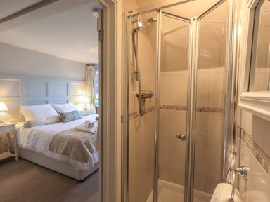 A bedroom with a bed and bedside tables visible next to a small tiled shower with glass doors at Wainwright Cottage in Ambleside