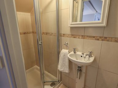 A bathroom with a corner shower enclosure a small sink with taps a towel ring with a towel and a mirror above the sink at Wainwright Cottage in Ambleside