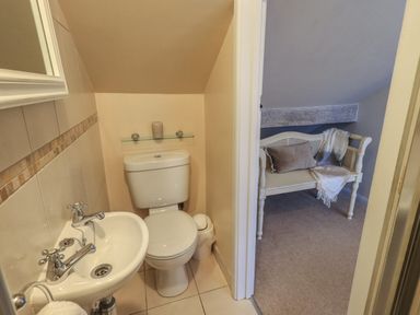 A small bathroom with toilet and sink next to a room with a white bench and cushions at Wainwright Cottage in Ambleside