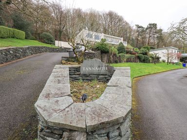 A stone sign reading Tannahiill beside a driveway with houses and trees in the background at Tanna Hill in Bowness