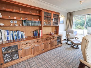 A room with a wooden bookshelf with books and ceramics a reclining chair a glass door and carpeted floor at Tanna Hill in Bowness