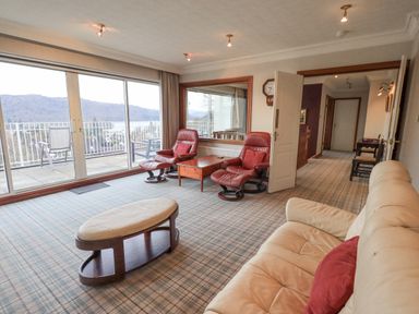 A living room with leather sofa and chairs near sliding glass doors and a balcony at Tanna Hill in Bowness