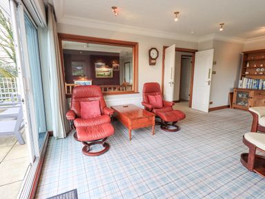 A sitting area with two red leather chairs a wooden table a glass door and a wooden bookshelf at Tanna Hill in Bowness