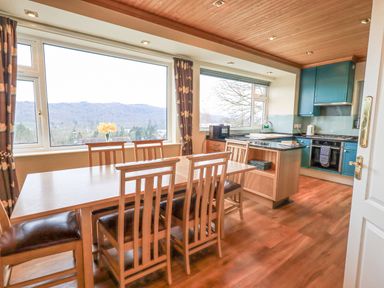 A dining area with wooden table and chairs next to large windows and a kitchen with teal cabinets and appliances at Tanna Hill in Bowness