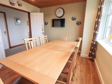 A dining room with a wooden table and six chairs a wall clock a television and decorated plates on the wall at Tanna Hill in Bowness