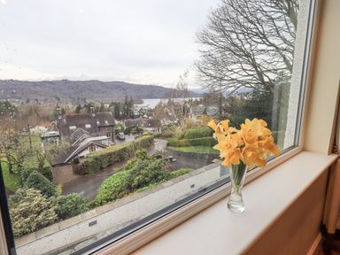 A vase with yellow flowers on a windowsill overlooking houses trees and hills at Tanna Hill in Bowness