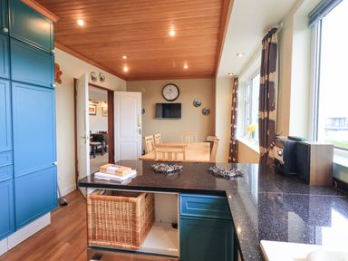 A kitchen with blue cabinets black countertops wooden dining table and chairs and windows with curtains at Tanna Hill in Bowness