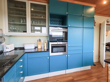 A kitchen with blue cabinets a built-in oven glass cabinets with glassware and a wooden floor at Tanna Hill in Bowness