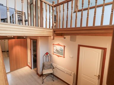 A hallway with a wooden railing above a chair and radiator with a painting on the wall at Tanna Hill in Bowness
