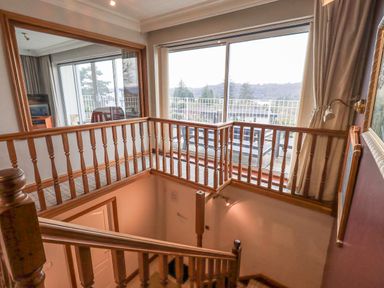 A staircase with wooden railings next to a large window and a wall mirror at Tanna Hill in Bowness