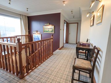 A hallway with a wooden railing a table chairs and framed pictures on the wall at Tanna Hill in Bowness