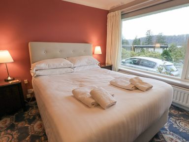 A bedroom with a bed with white linens and towels on it bedside tables with lamps and a large window showing a car outside at Tanna Hill in Bowness