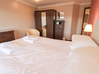 A bedroom with a bed with folded towels a wardrobe a chest of drawers and a chair at Tanna Hill in Bowness