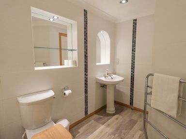 A bathroom with a toilet wooden seat pedestal sink towel rack with white towel and tiled walls at Tanna Hill in Bowness