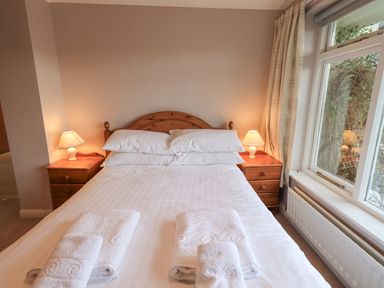 A bedroom with a bed with white linens and towels on it two bedside tables with lamps and a window with curtains at Tanna Hill in Bowness