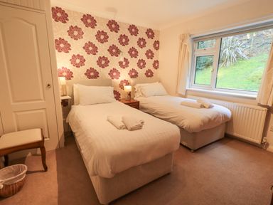 A bedroom with two single beds bedside tables lamps a window and floral wallpaper at Tanna Hill in Bowness