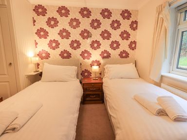 A bedroom with two single beds separated by a nightstand with lamps and a window with curtains at Tanna Hill in Bowness