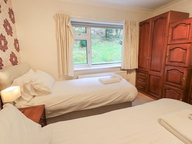 A bedroom with two single beds a wooden nightstand with a lamp a large window with curtains and a wooden wardrobe at Tanna Hill in Bowness