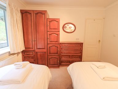 A bedroom with two beds with white linens and towels wooden cabinets and a door at Tanna Hill in Bowness