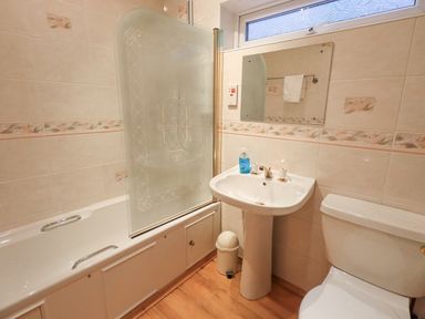 A bathroom with a bathtub with a frosted glass shower screen a pedestal sink with hand soap a mirror above and a toilet at Tanna Hill in Bowness