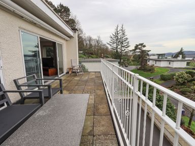 A balcony with outdoor chairs and table overlooking trees and modern houses at Tanna Hill in Bowness