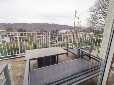 A balcony with outdoor furniture and a view of hills trees and houses at Tanna Hill in Bowness