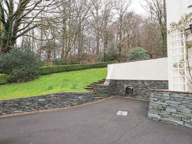 An outdoor space with stone retaining walls stairs green grass and trees at Tanna Hill in Bowness