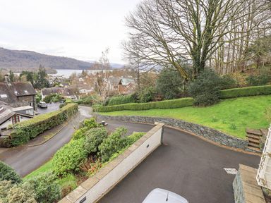 A sloped driveway with trimmed hedges and a large tree overlooking houses and a lake at Tanna Hill in Bowness