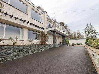 A driveway leading to a house with large windows stone walls and a balcony at Tanna Hill in Bowness