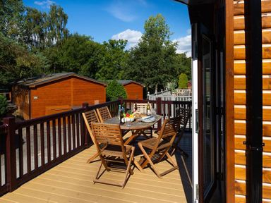A wooden deck with a table and chairs set with food and drinks outside wooden cabins at Lancashire Rose in Ambleside