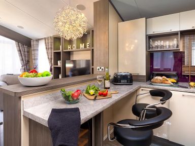 A kitchen area with a countertop and two black chairs a fruit bowl glass bowl with vegetables and a bottle of wine at Lancashire Rose in Ambleside