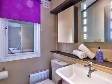 A bathroom with a sink toilet mirror and window with a purple blind at Lancashire Rose in Ambleside
