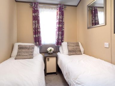 A bedroom with two single beds separated by a nightstand with flowers under a window with patterned curtains at Lancashire Rose in Ambleside